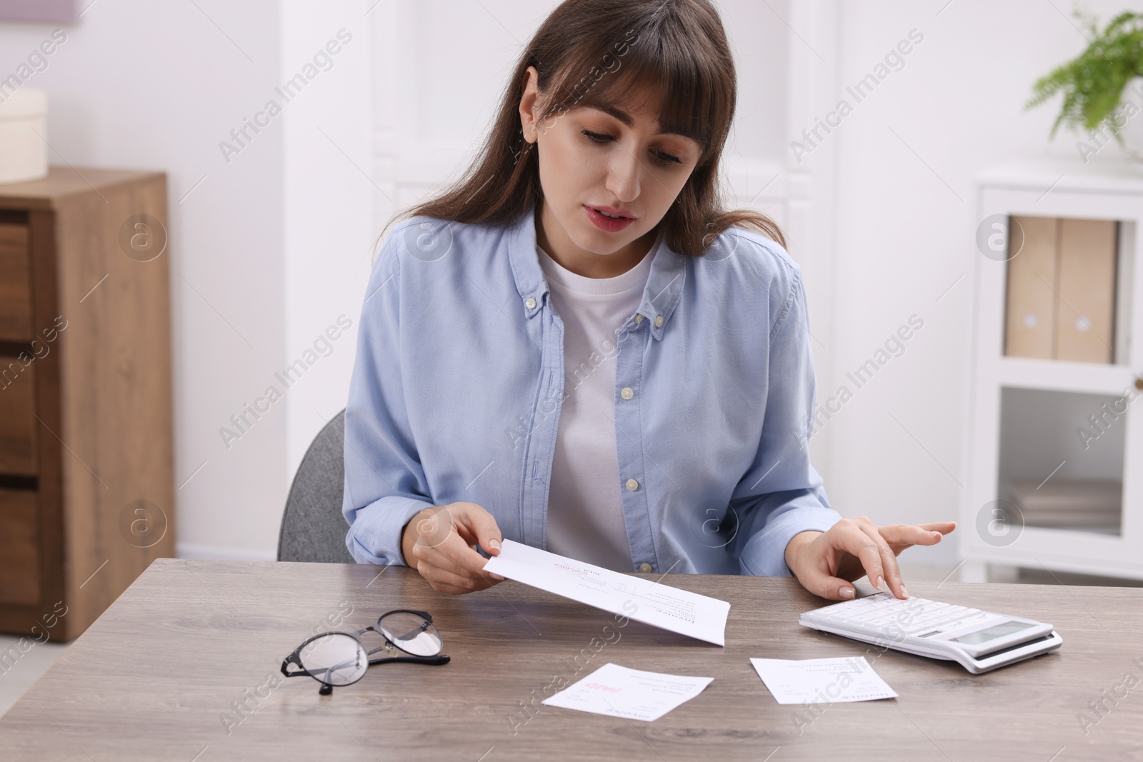 Photo of Paying bills. Woman with different invoices and calculator at wooden table indoors