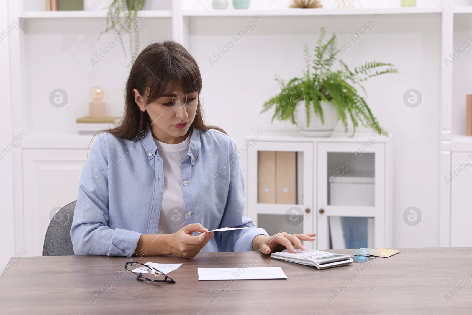 Photo of Paying bills. Woman with different invoices and calculator at wooden table indoors