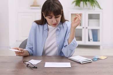 Photo of Paying bills. Woman with different invoices and calculator at wooden table indoors