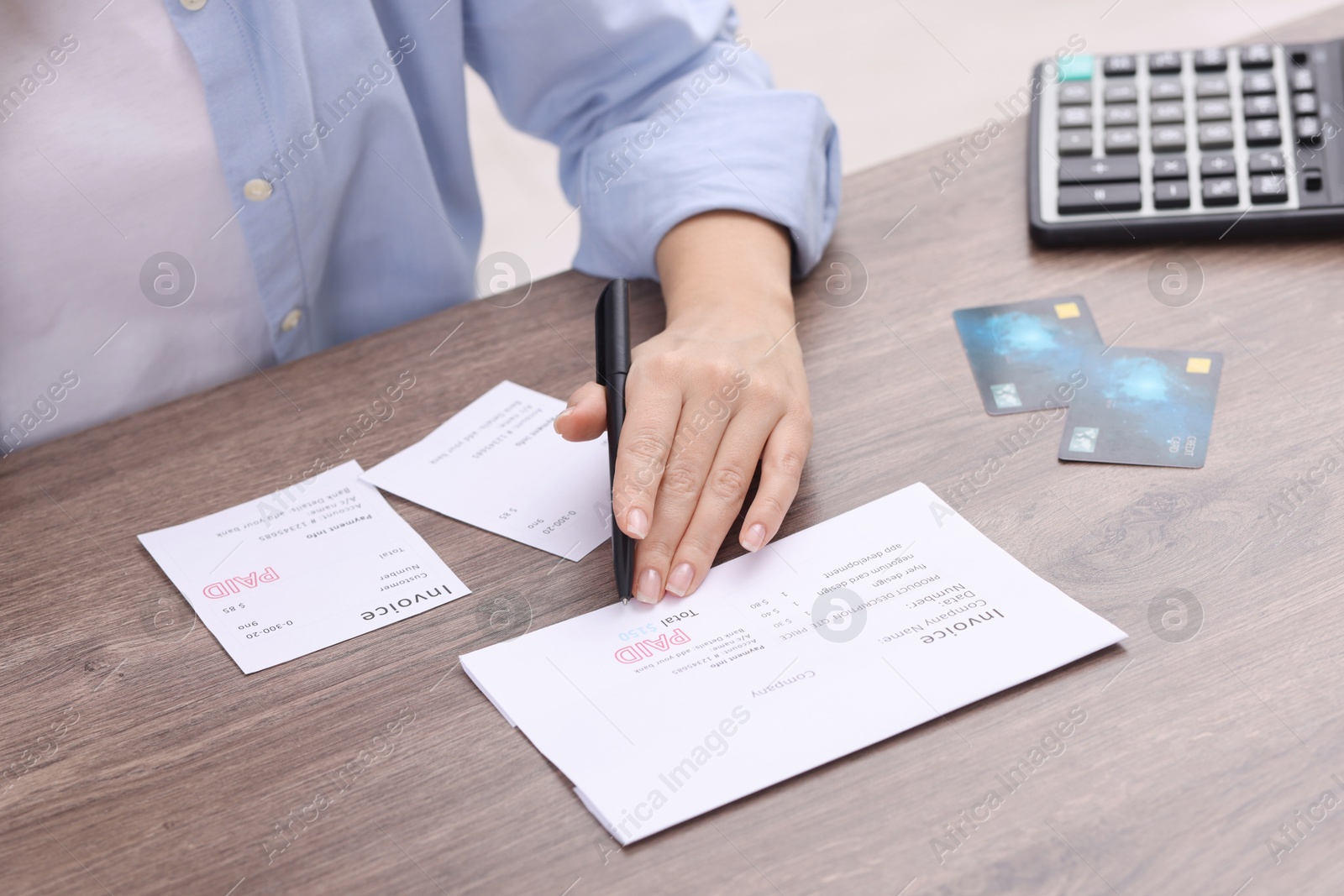 Photo of Paying bills. Woman with different invoices, credit cards and calculator at wooden table indoors, closeup