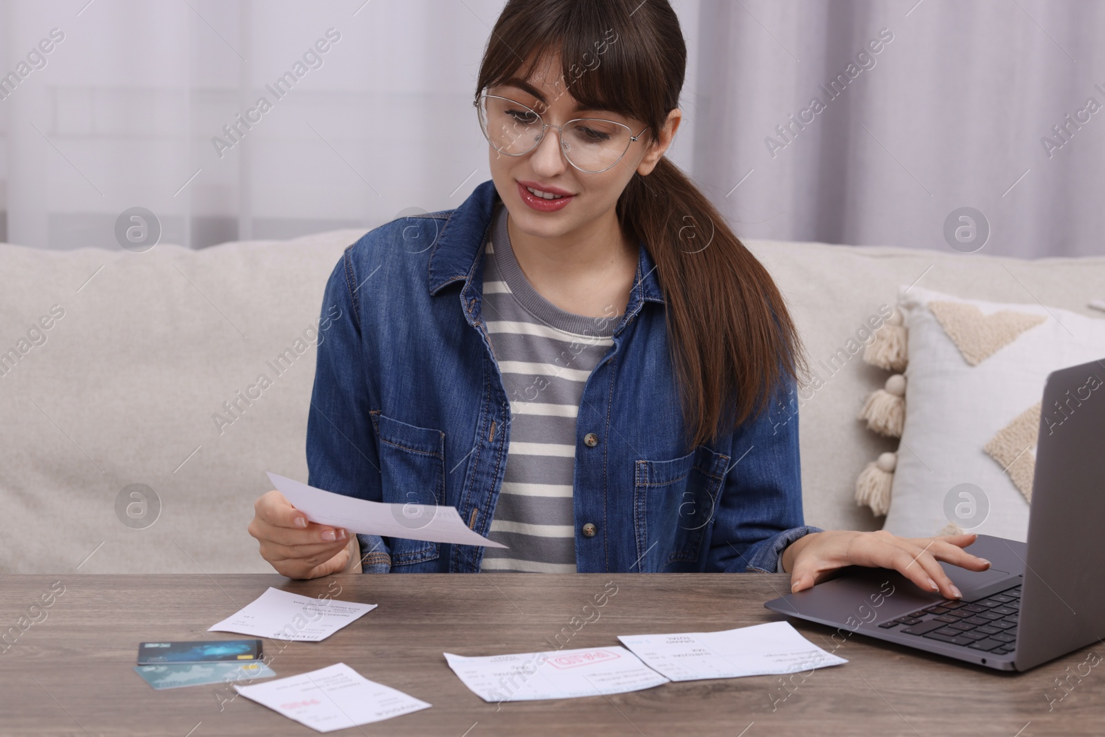 Photo of Paying bills. Woman with different invoices, credit cards and laptop at wooden table indoors