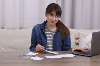 Photo of Paying bills. Woman with different invoices, credit cards and laptop at wooden table indoors