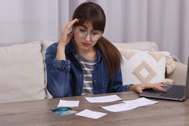 Paying bills. Upset woman with different invoices, credit cards and laptop at wooden table indoors