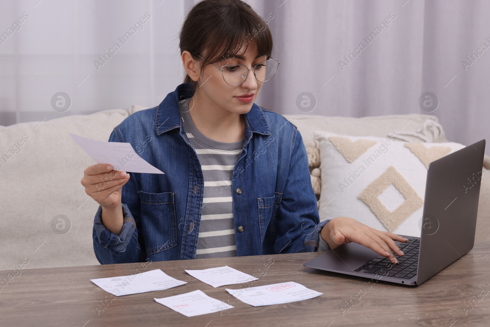 Photo of Paying bills. Woman with different invoices and laptop at wooden table indoors