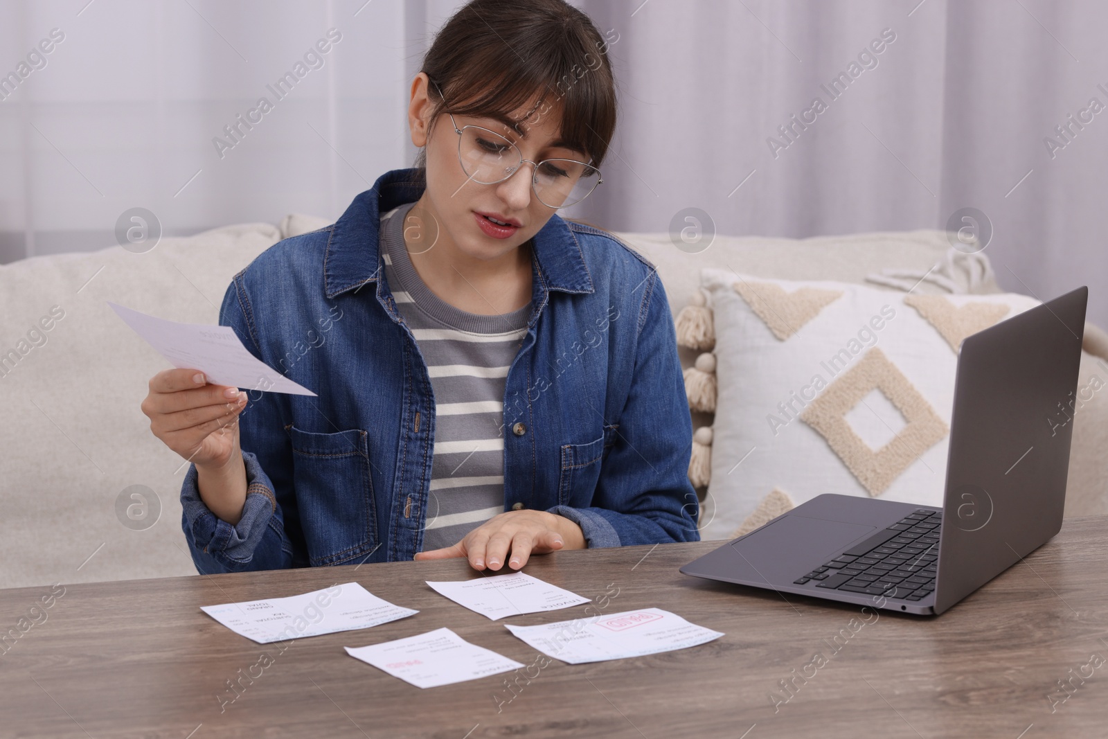 Photo of Paying bills. Woman with different invoices and laptop at wooden table indoors