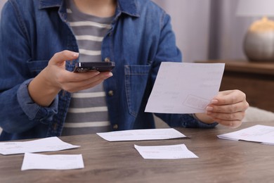 Photo of Paying bills. Woman with different invoices and phone at wooden table indoors, closeup