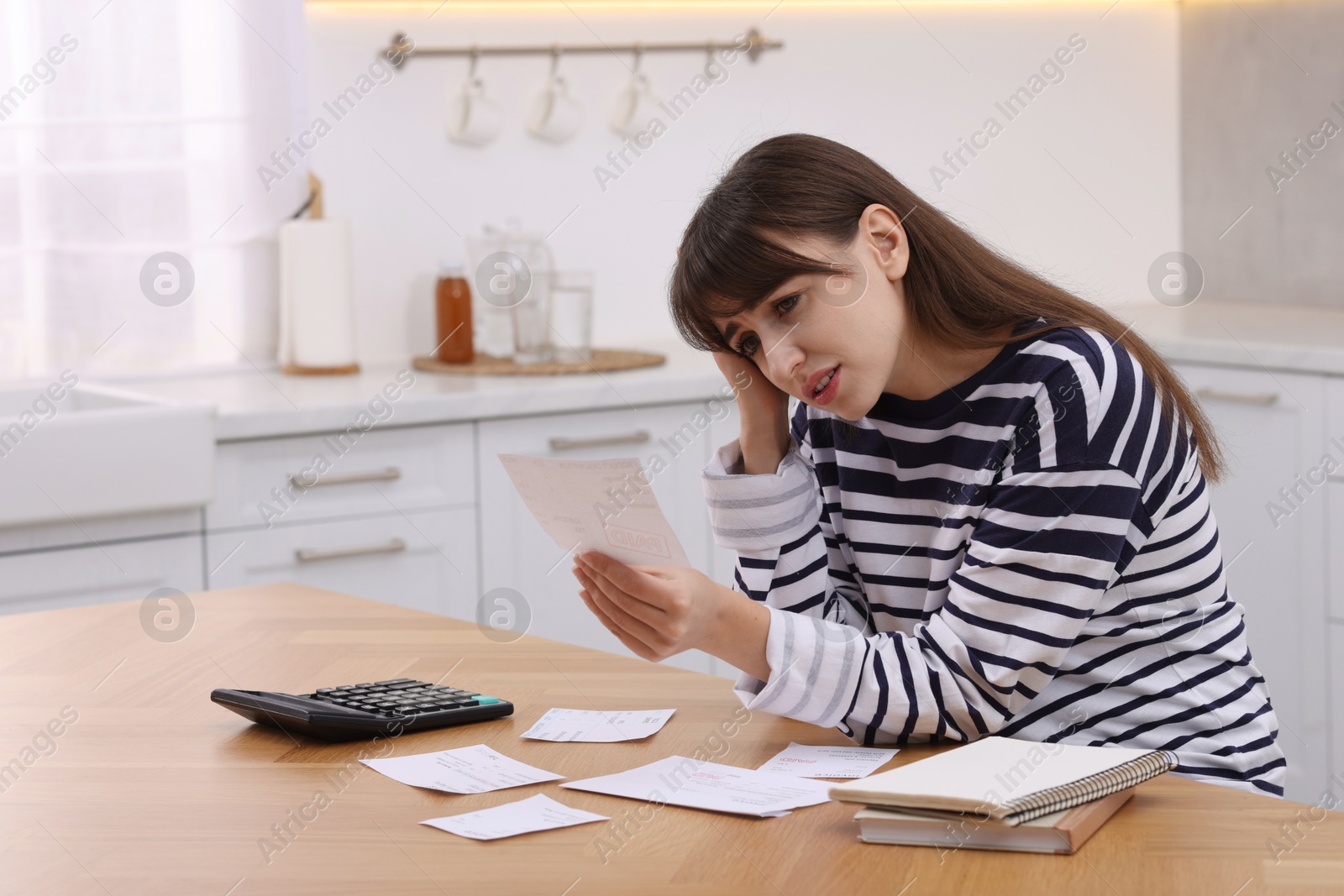 Photo of Paying bills. Upset woman with different invoices and calculator at wooden table indoors