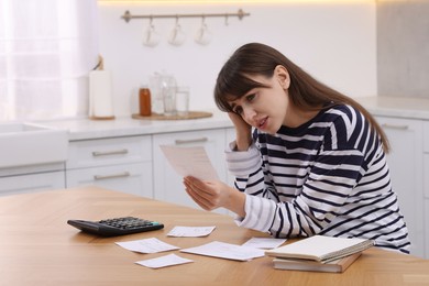 Paying bills. Upset woman with different invoices and calculator at wooden table indoors