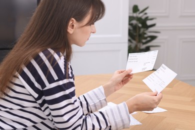 Photo of Paying bills. Woman with different invoices at wooden table indoors