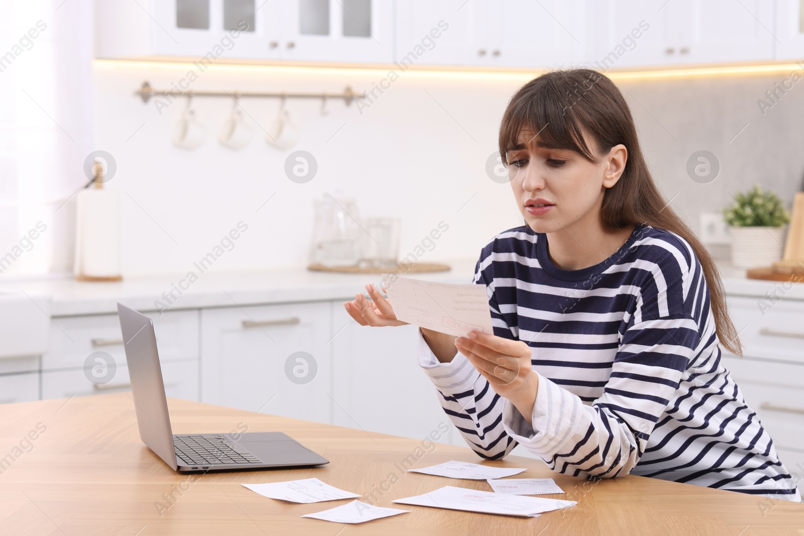 Photo of Paying bills. Upset woman with different invoices and laptop at wooden table indoors