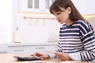 Photo of Paying bills. Woman with different invoices and calculator at wooden table indoors, space for text