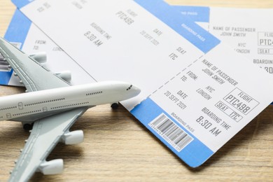 Photo of Travel agency. Flight tickets and plane model on wooden table, closeup