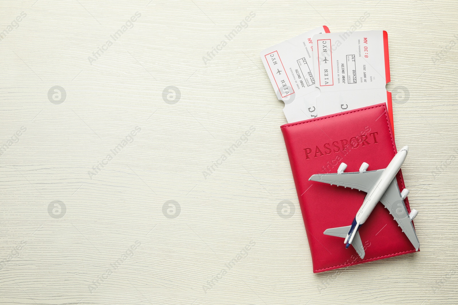 Photo of Travel agency. Flight tickets, passport and plane model on light wooden table, top view. Space for text