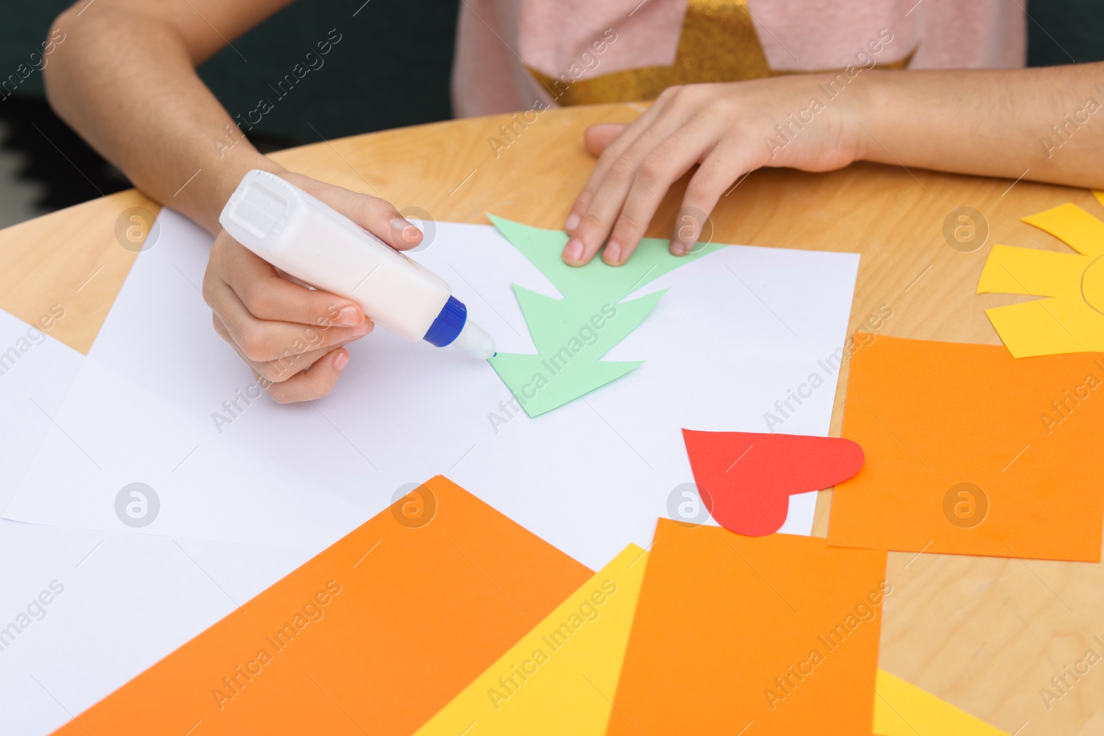 Photo of Girl applying glue onto paper figure for her creative project at table indoors, closeup. Art and craft