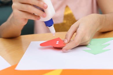 Photo of Girl applying glue onto paper figure for her creative project at table indoors, closeup. Art and craft