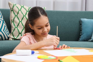 Photo of Girl applying glue onto paper figure for her creative project at table indoors. Art and craft