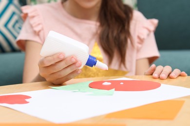 Photo of Girl applying glue onto paper figure for her creative project at table indoors, closeup. Art and craft