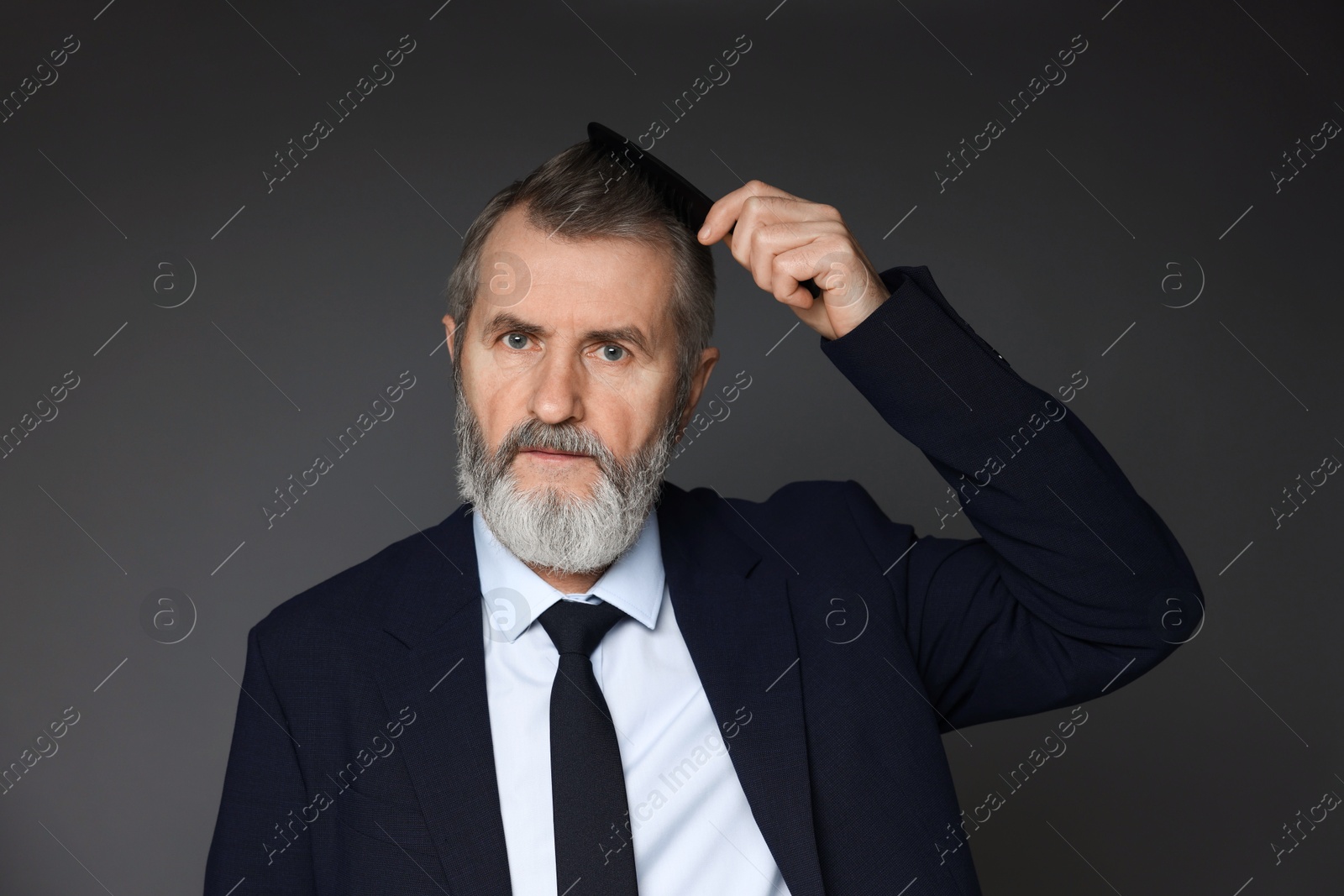 Photo of Handsome man combing his hair on dark grey background