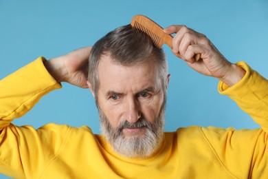 Photo of Handsome man combing his hair on light blue background