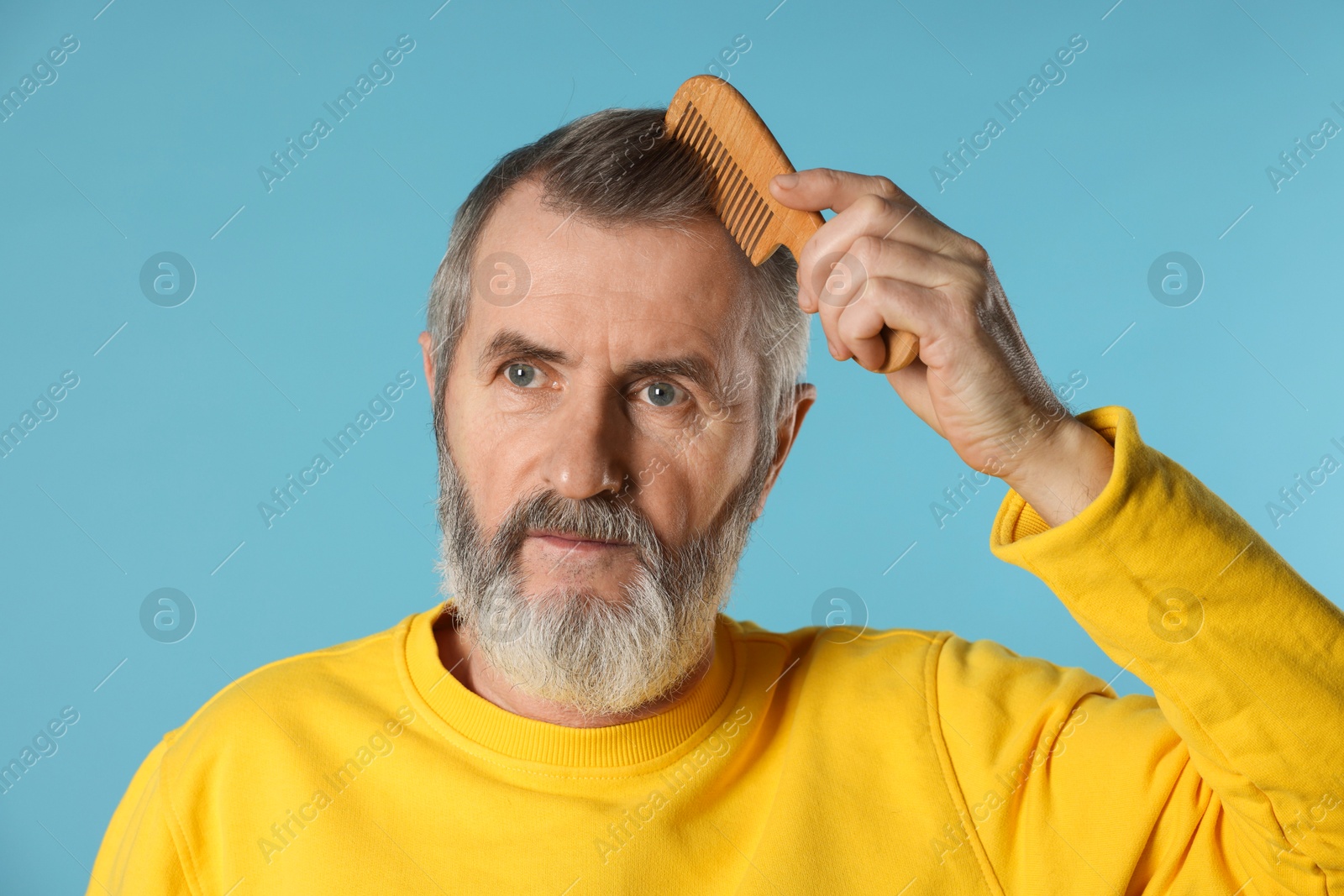 Photo of Handsome man combing his hair on light blue background