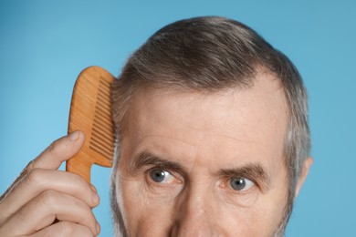 Photo of Man combing his hair on light blue background, closeup