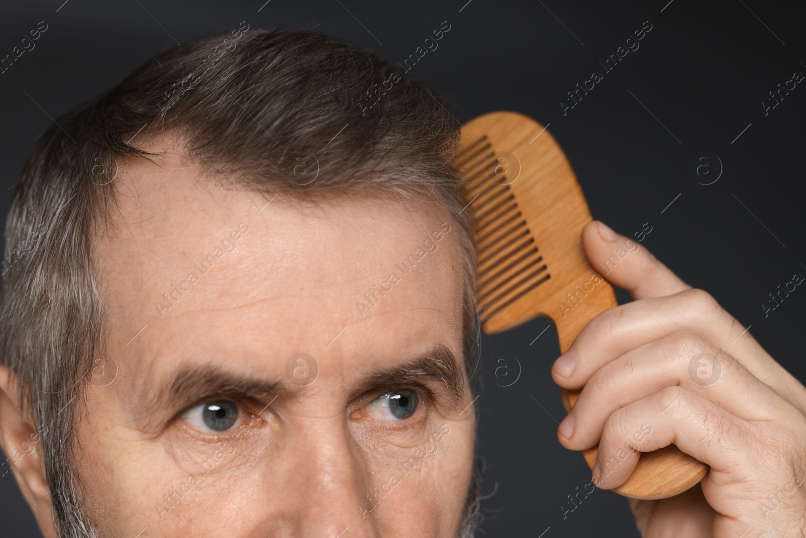 Photo of Man combing his hair on dark grey background, closeup