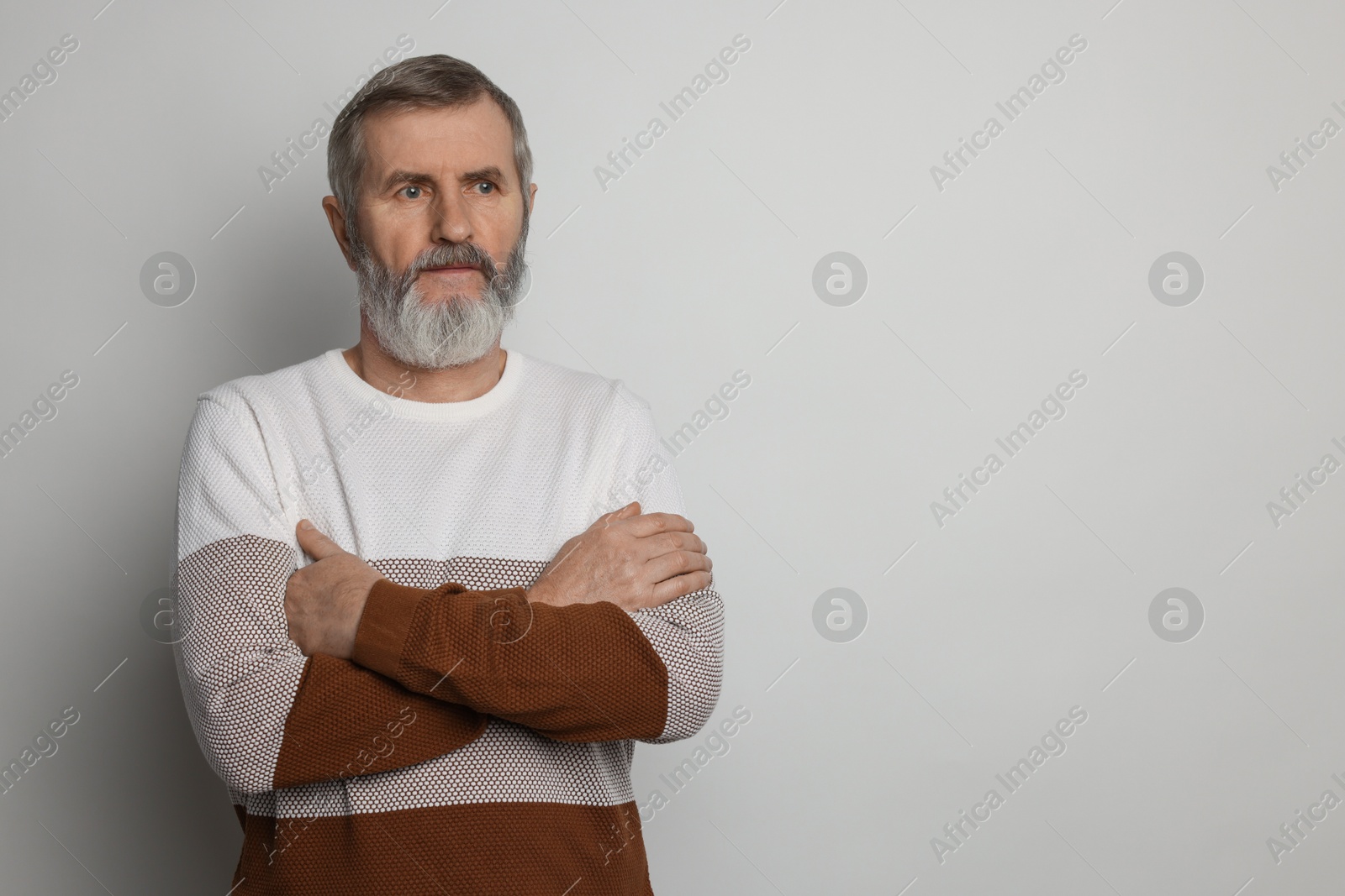 Photo of Portrait of mature man with crossed arms on light grey background, space for text