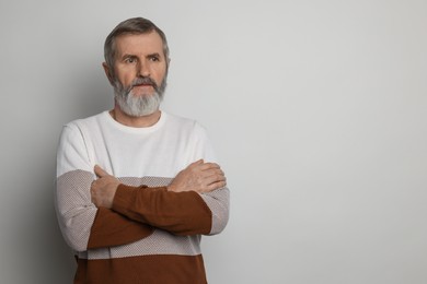 Photo of Portrait of mature man with crossed arms on light grey background, space for text