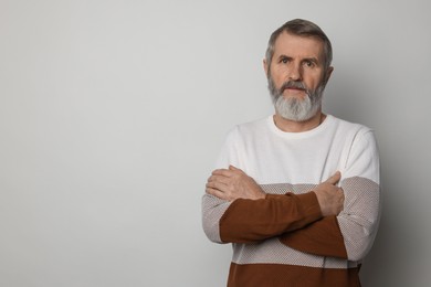 Photo of Portrait of mature man with crossed arms on light grey background, space for text