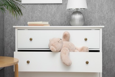 Photo of Teddy bear in open drawer of dresser in room