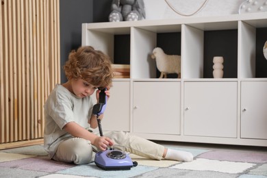 Photo of Cute little boy with telephone on floor indoors, space for text