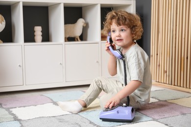 Photo of Cute little boy with telephone on floor indoors, space for text