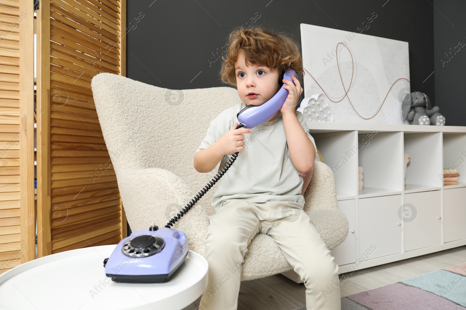 Photo of Cute little boy with telephone in armchair indoors