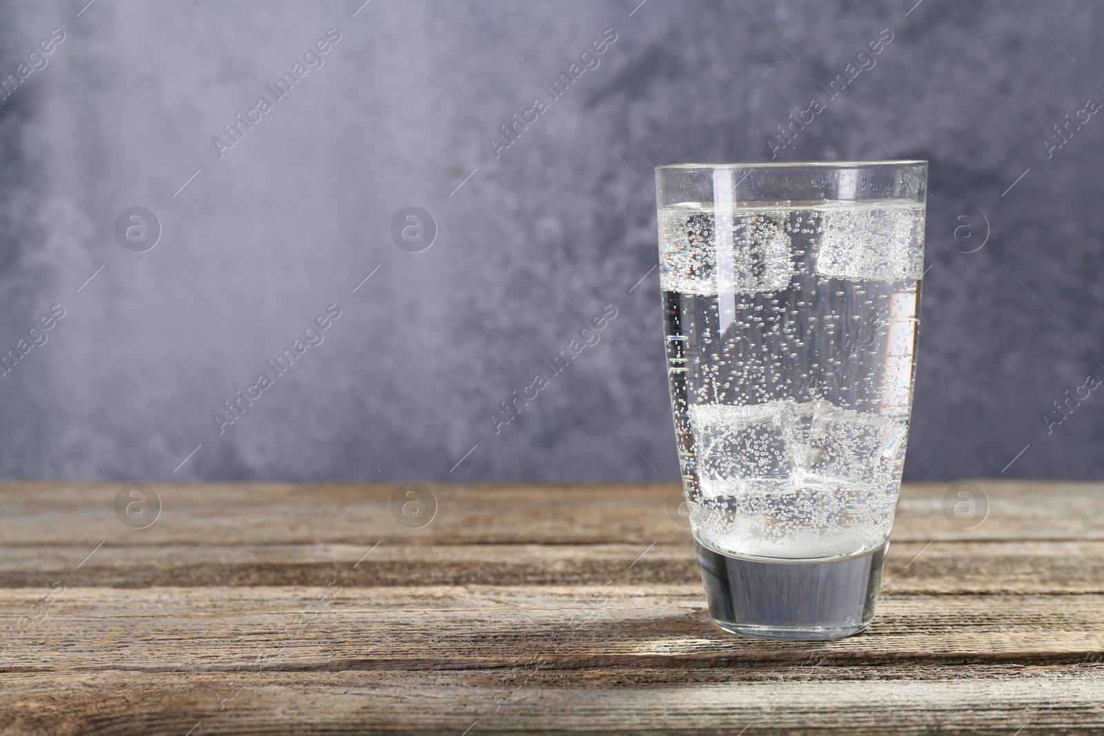 Photo of Soda water with ice cubes in glass on wooden table, space for text