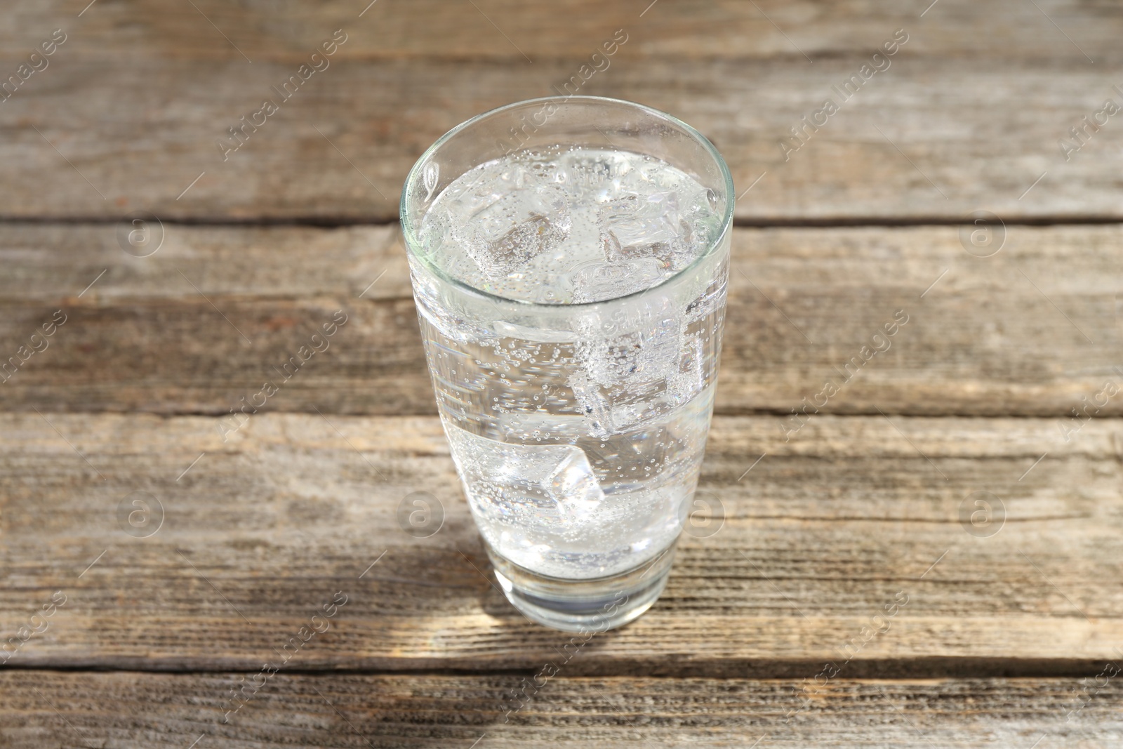 Photo of Soda water with ice cubes in glass on wooden table, closeup