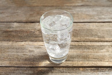 Photo of Soda water with ice cubes in glass on wooden table, closeup