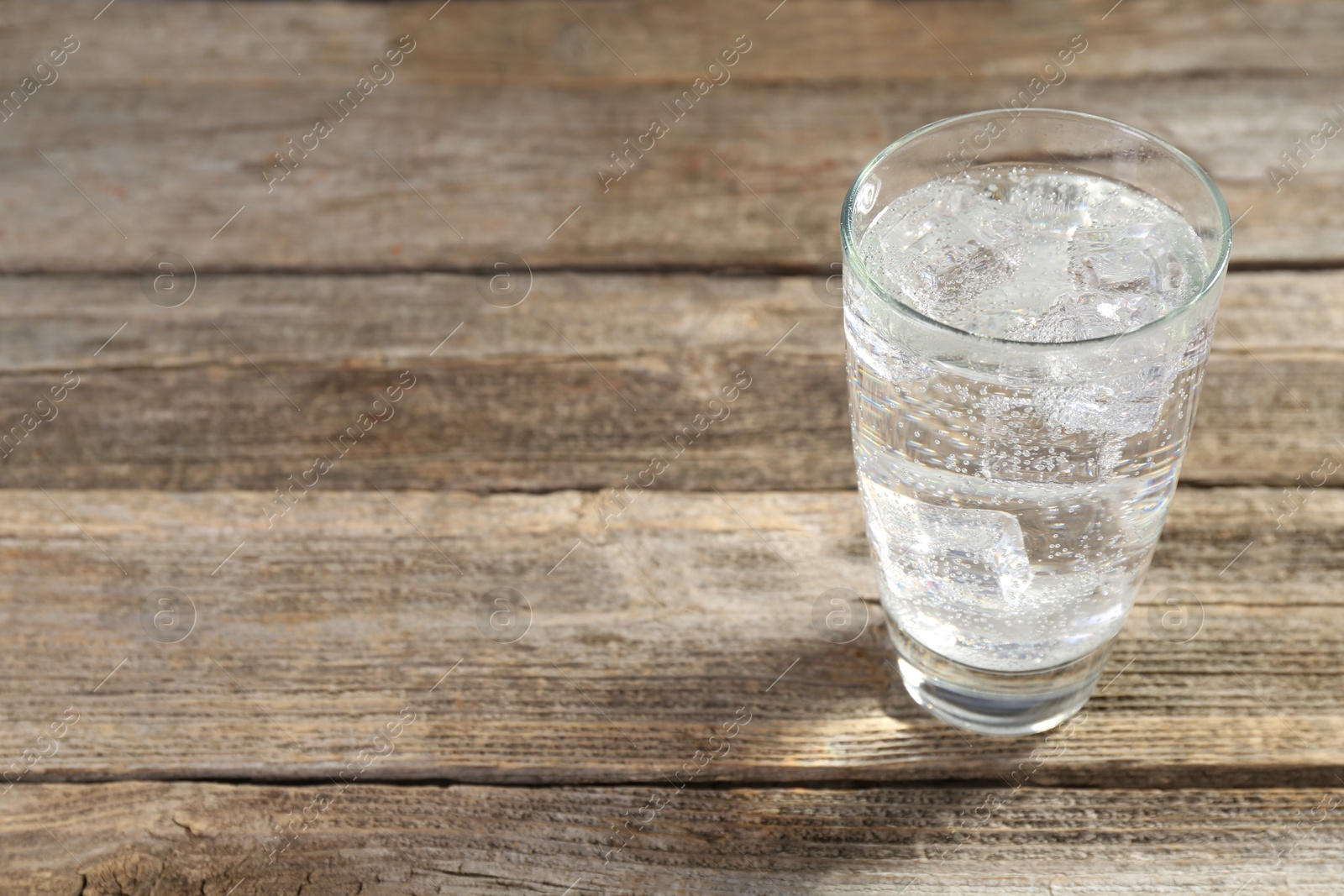 Photo of Soda water with ice cubes in glass on wooden table, closeup. Space for text