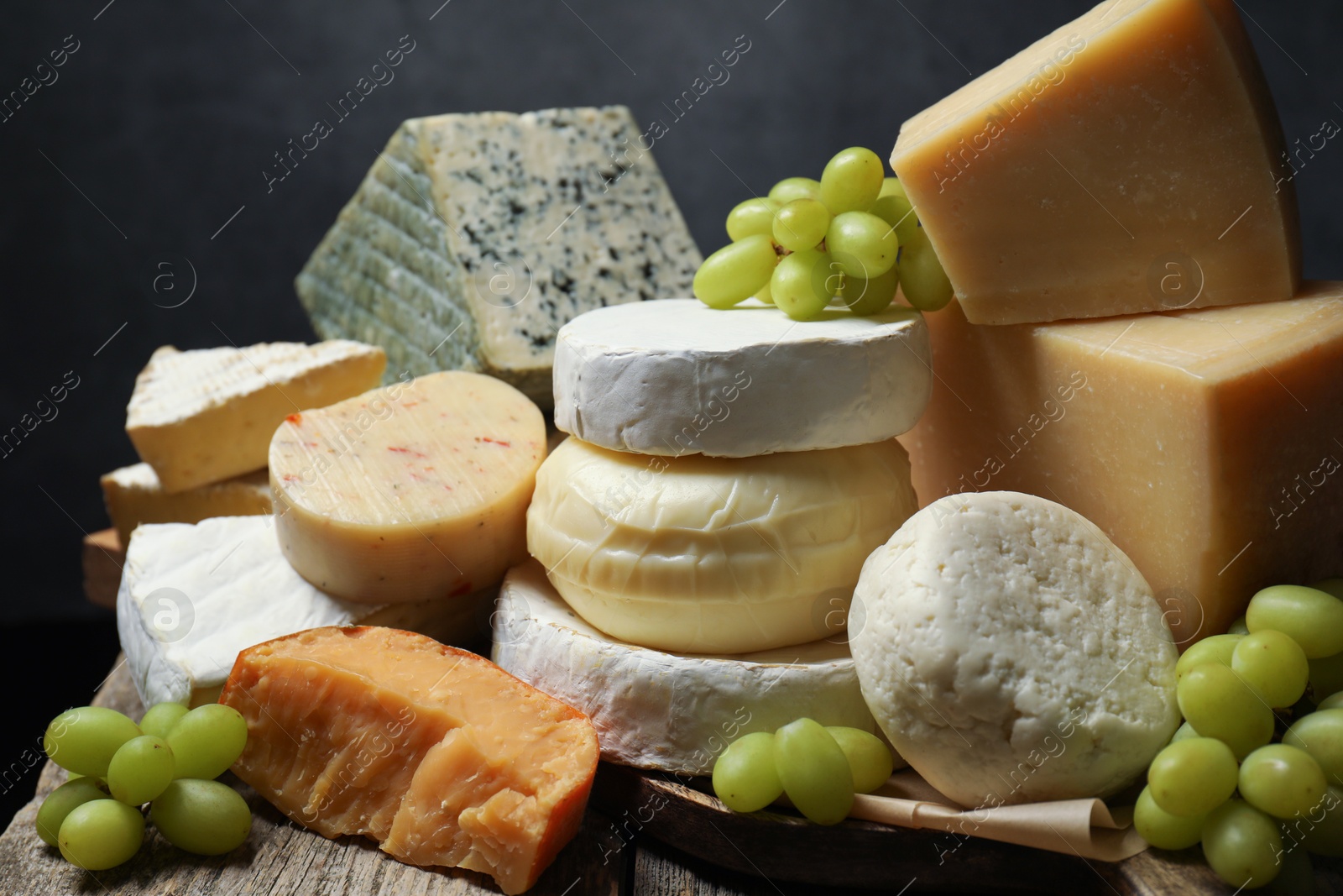 Photo of Different types of cheese and grapes on wooden table against dark background, closeup