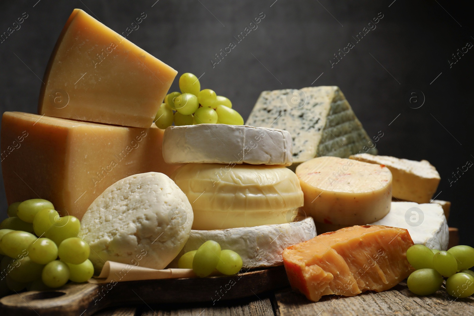 Photo of Different types of cheese and grapes on wooden table against dark background, closeup