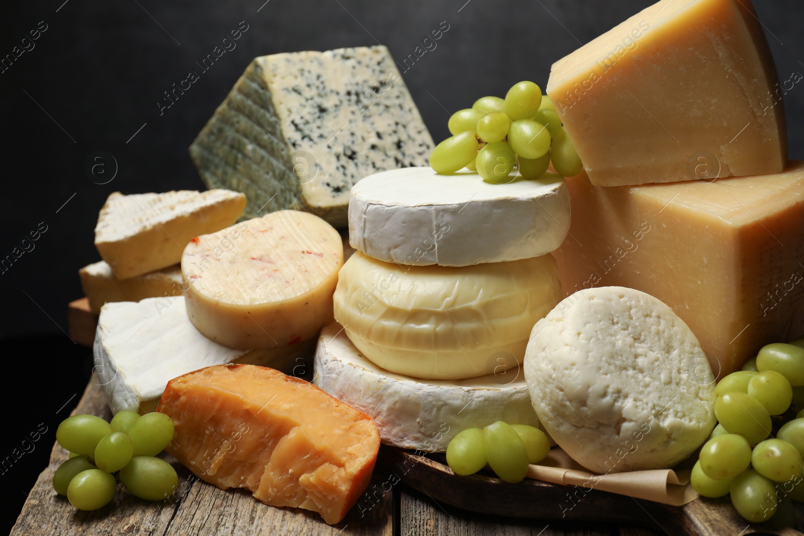 Photo of Different types of cheese and grapes on wooden table against dark background, closeup