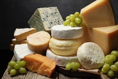 Photo of Different types of cheese and grapes on wooden table against dark background, closeup