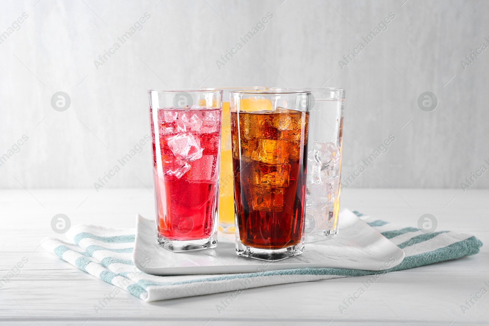 Photo of Soda water of different flavors with ice cubes in glasses on white wooden table