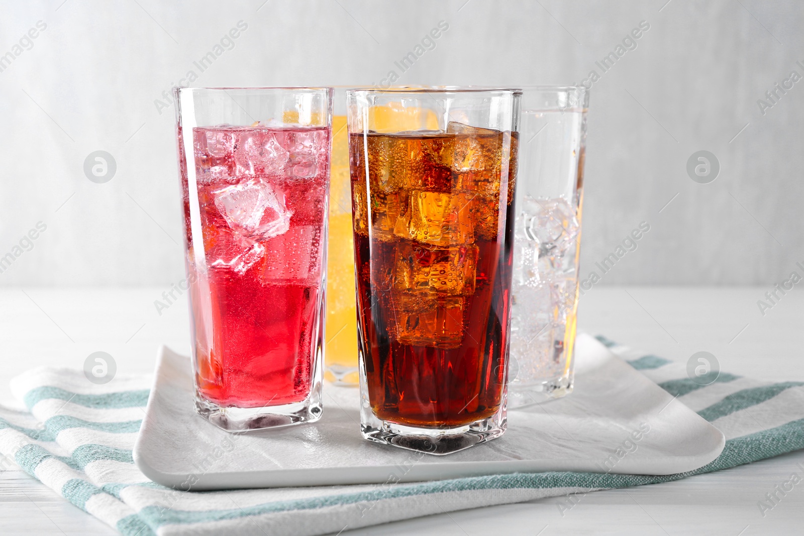 Photo of Soda water of different flavors with ice cubes in glasses on white wooden table