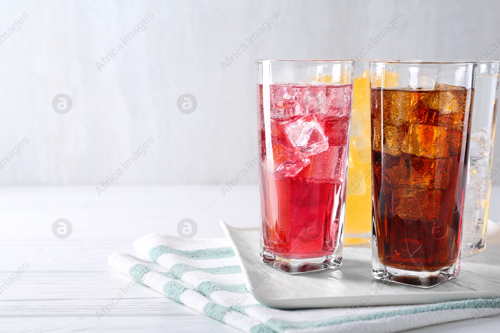 Photo of Soda water of different flavors with ice cubes in glasses on white wooden table, space for text