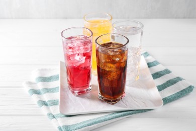 Photo of Soda water of different flavors with ice cubes in glasses on white wooden table