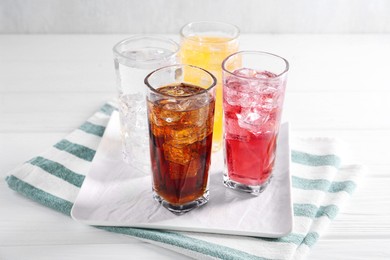 Photo of Soda water of different flavors with ice cubes in glasses on white wooden table