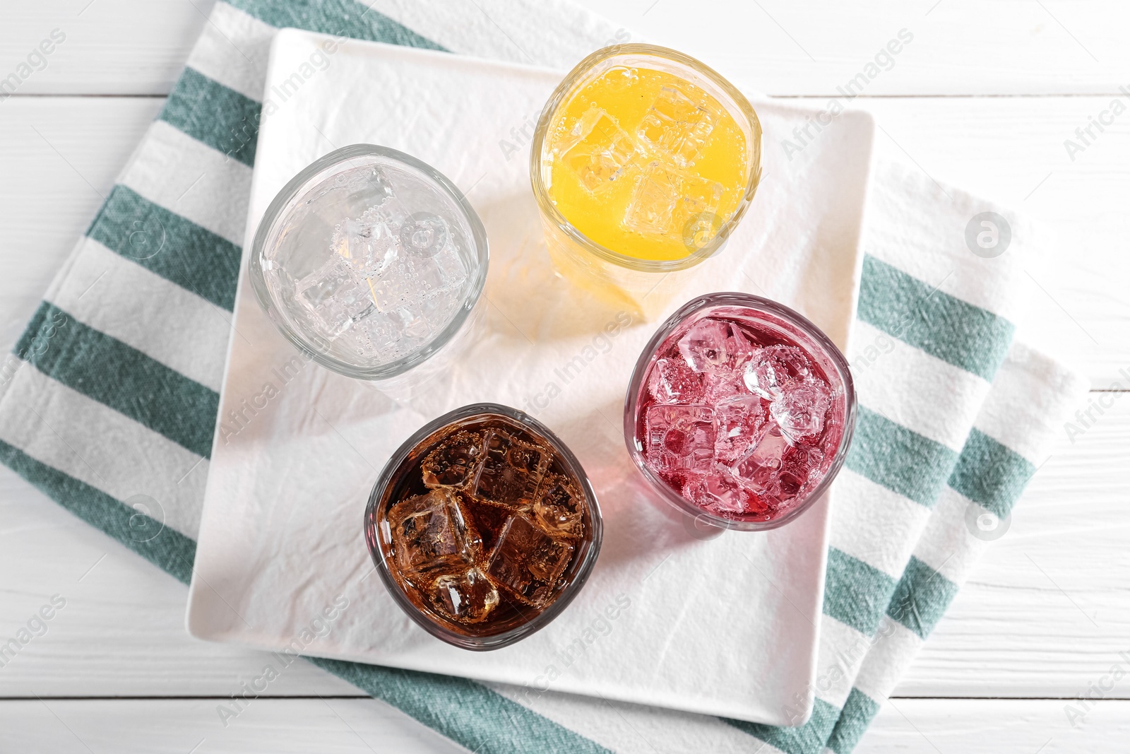 Photo of Soda water of different flavors with ice cubes in glasses on white wooden table, top view