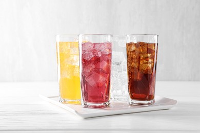 Photo of Soda water of different flavors with ice cubes in glasses on white wooden table