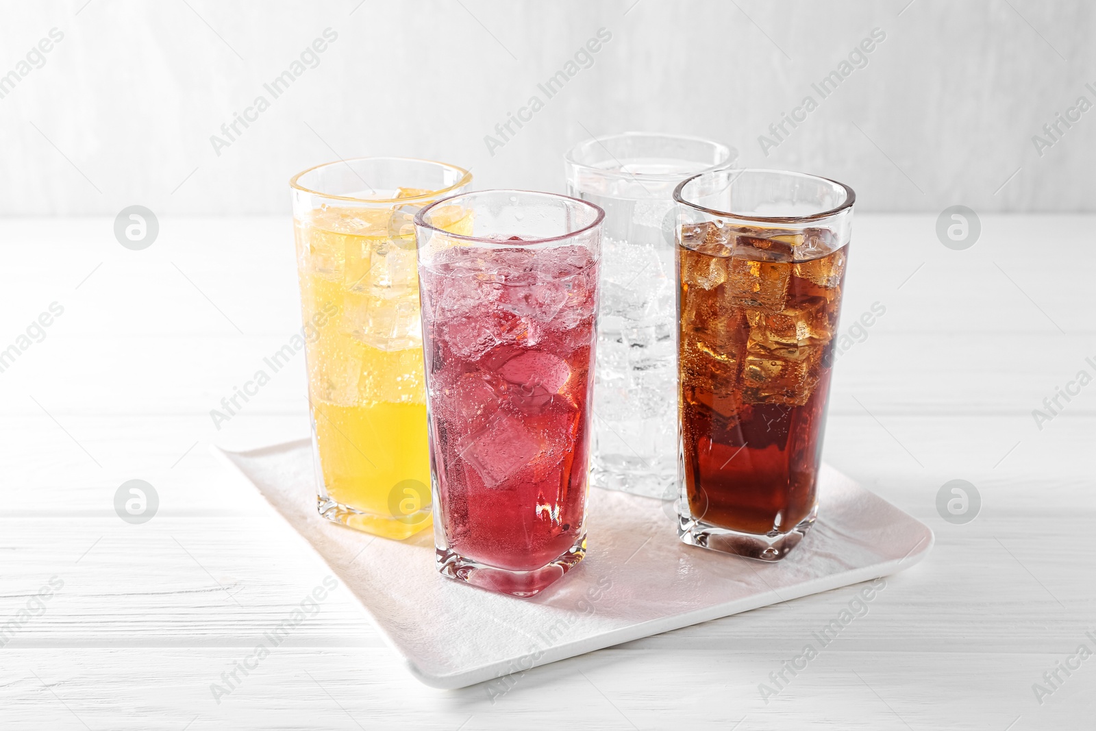 Photo of Soda water of different flavors with ice cubes in glasses on white wooden table