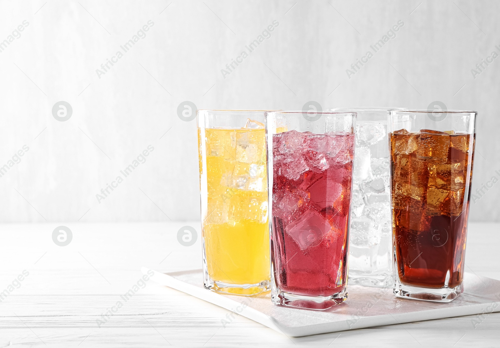 Photo of Soda water of different flavors with ice cubes in glasses on white wooden table, space for text